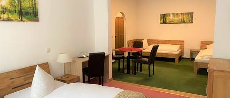 Habitación de hotel con cama, un escritorio con silla, una mesita de noche con lámpara y dos cuadros en las paredes.