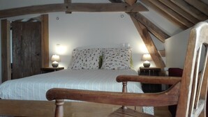 A bedroom with a sloped ceiling, a bed with striped bedding, two bedside lamps, and a wooden chair. - Ferme de Bellevue (Landes-le-Gaulois)