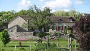A stone building with a sloped roof, a wooden fence, and a garden with pink flowers. - Ferme de Bellevue (Landes-le-Gaulois)