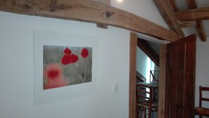 A room with a wooden ceiling beam, a white wall with a framed picture, and a door leading to another room. - Ferme de Bellevue (Landes-le-Gaulois)