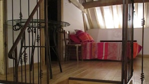 A loft bedroom with a wooden staircase, a bed with patterned bedding, and a window with natural light. - Ferme de Bellevue (Landes-le-Gaulois)