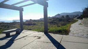 Um caminho de pedra leva a um banco com vista para o mar e colinas ao fundo.