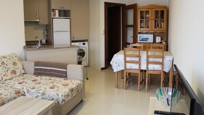 Espaço compacto com sofá, mesa de jantar com cadeiras, cozinha equipada com frigorífico e micro-ondas, e máquina de lavar roupa.