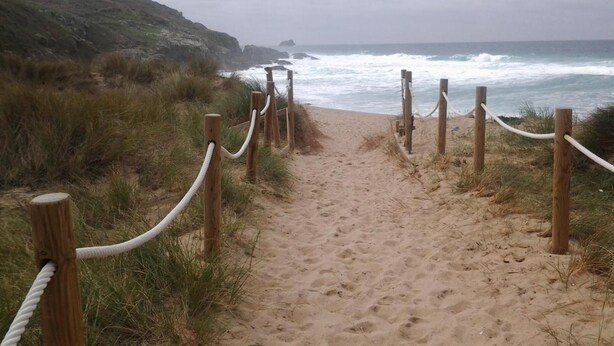 Uma trilha de areia com postes de madeira e cordas brancas, que leva ao oceano.