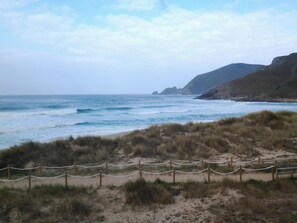 A coastal landscape with a sandy beach, grassy dunes, and a wooden fence. - Pensión San Roque (Lugo)