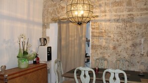 Un comedor con pared de piedra, una araña, una mesa de madera y sillas blancas.