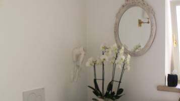 A bathroom with a white toilet, a sink with a round basin, a mirror with an ornate frame, and a potted orchid plant.