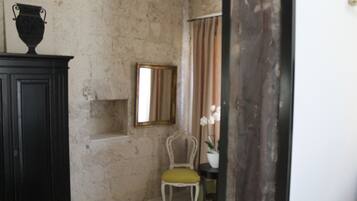 Une pièce avec un mur en pierre, une armoire en bois, une chaise avec un coussin, un miroir et une plante en pot.