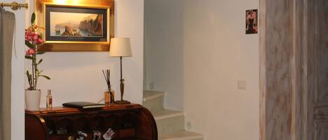 A room with a desk, a framed picture, a lamp, and a staircase.