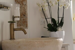 A bathroom with a white sink, a brass faucet, and a white vase with white orchids.