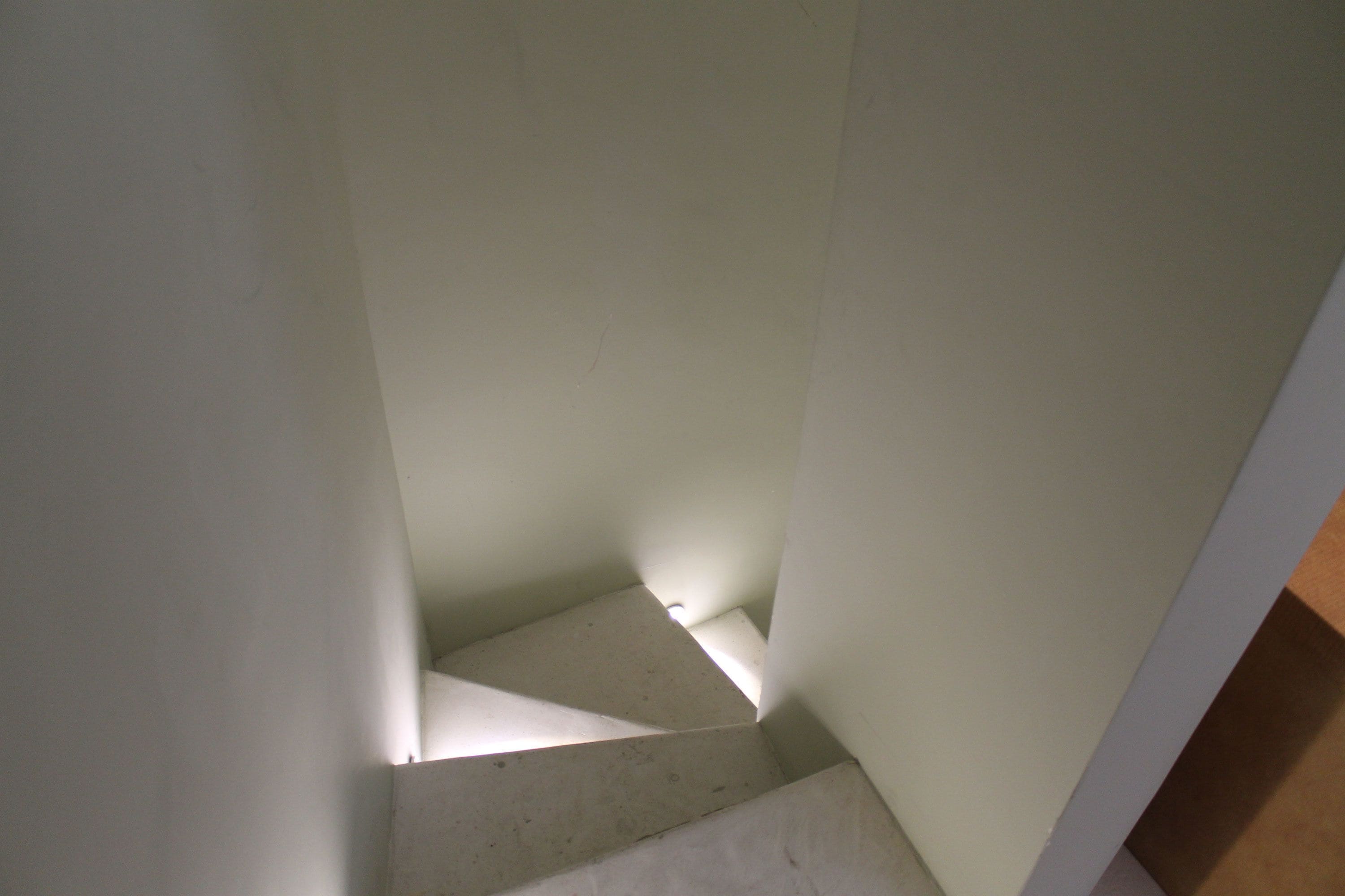 Eine schmale Treppe mit weißen Wänden und einem hölzernen Geländer.