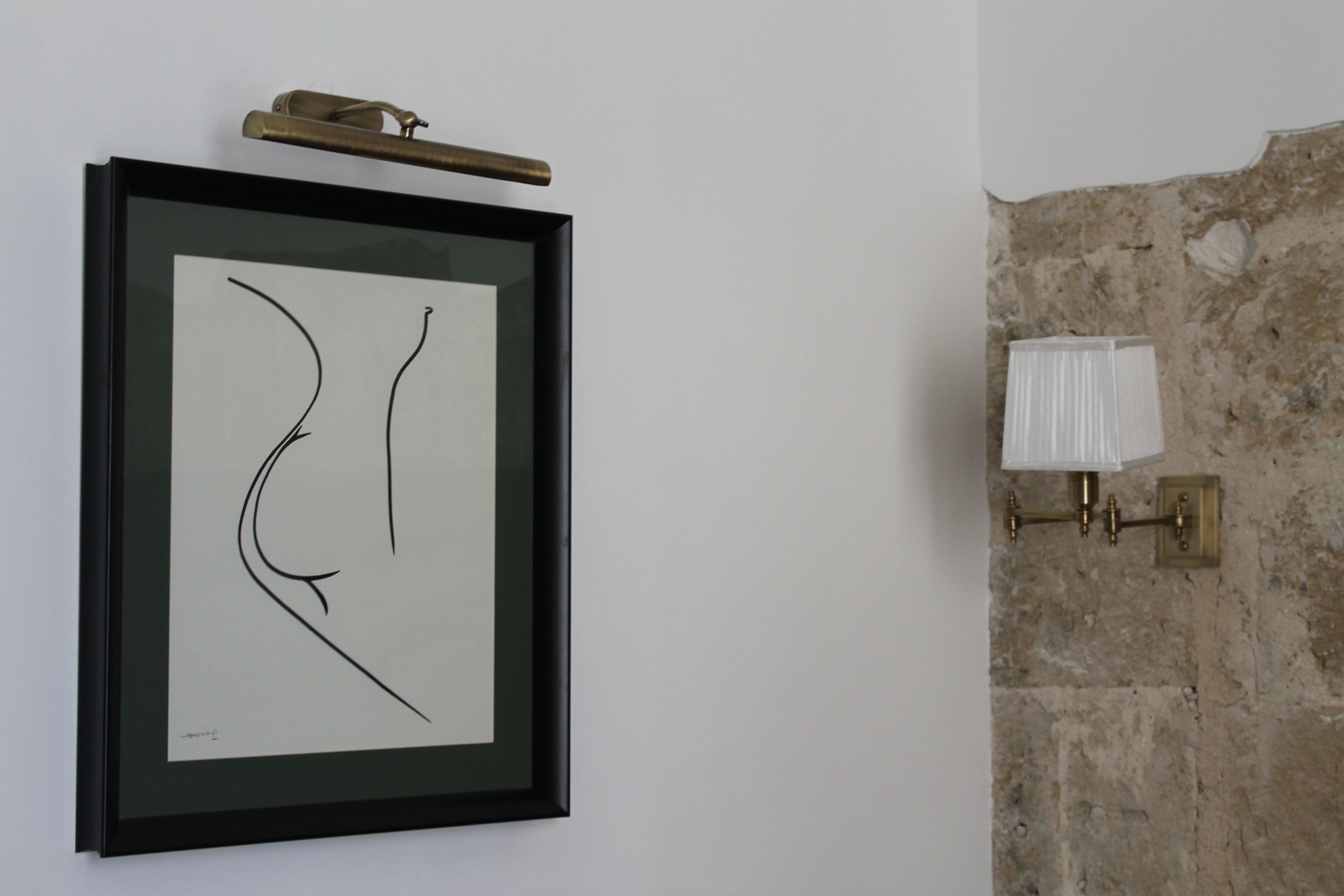 A framed abstract artwork on a white wall, a brass light fixture, and a textured stone wall.