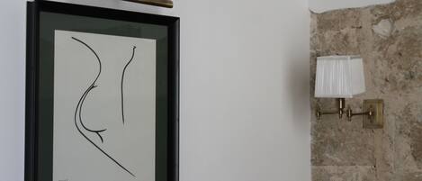 A framed abstract artwork on a white wall, a brass light fixture, and a textured stone wall.