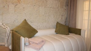 Una cama con colcha blanca, dos almohadas verdes y una toalla doblada.