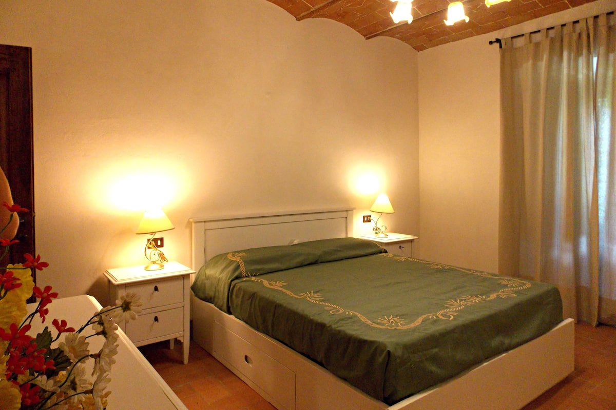 Quarto com uma cama, duas mesas de cabeceira com abajures, um criado-mudo e uma janela com cortinas.