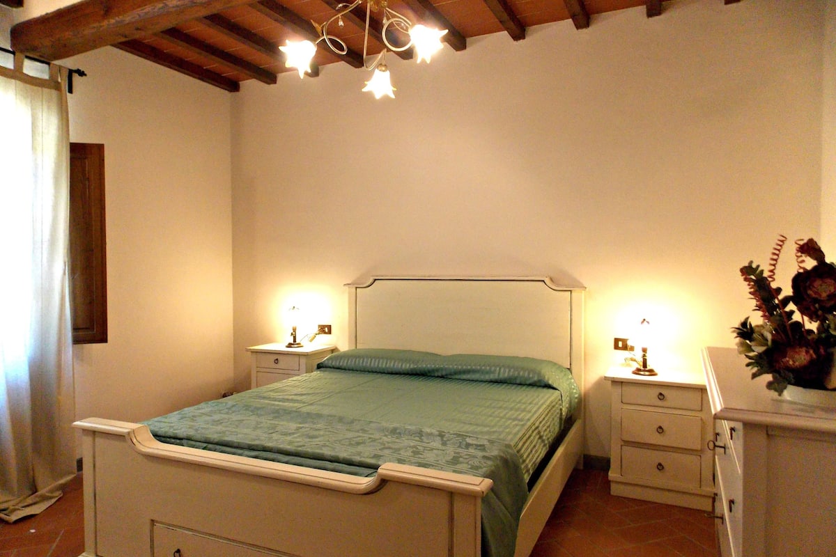 Quarto com cama, duas mesinhas de cabeceira, cômoda e lustre.