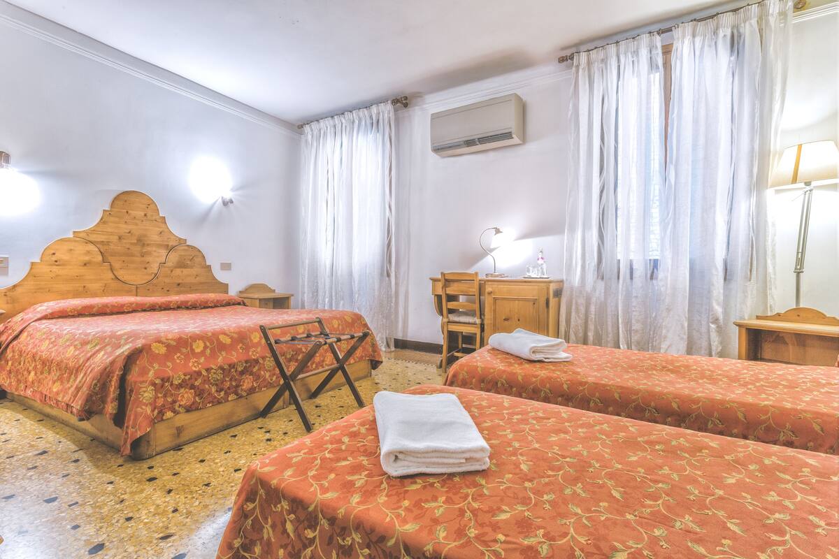 A hotel room with two beds, a wooden headboard, a desk, a chair, and a lamp.