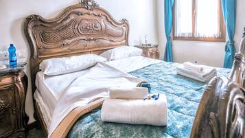 Un lit bien fait, recouvert d’une couvre-lit bleue à motifs, avec une tête de lit en bois ornée de sculptures complexes, et une table de chevet sur laquelle se trouvent une bouteille bleue et une bouteille blanche.