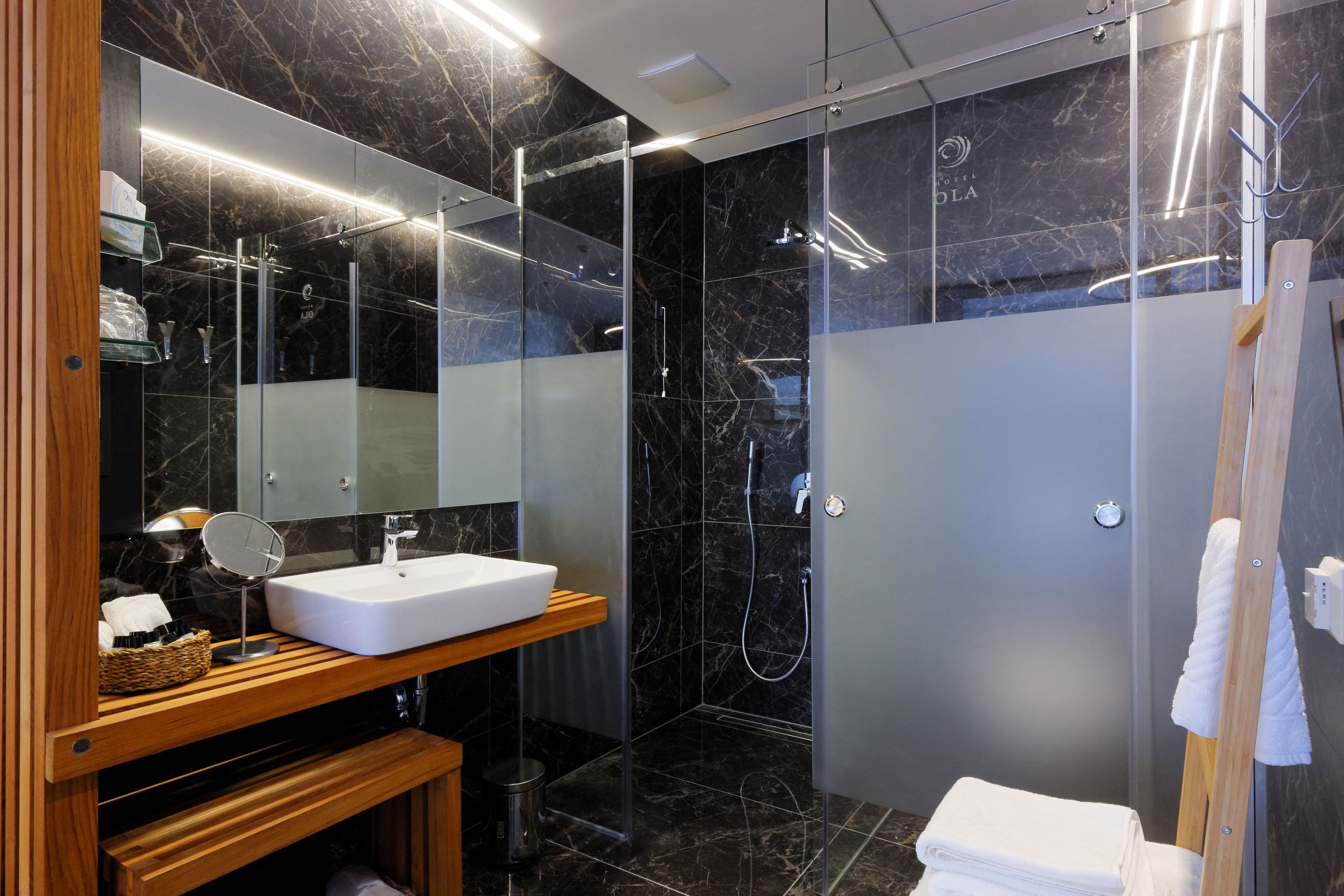 A modern bathroom with a marble shower, a wooden vanity, and a large mirror.