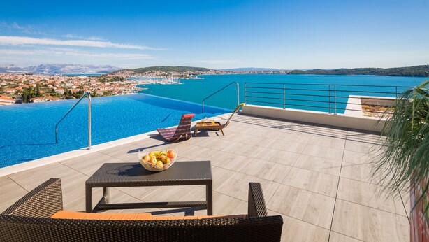 Una piscina en la azotea con agua cristalina y vistas a un pueblo costero, además de sillones de descanso.