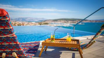 A poolside area with a wooden table, two drinks, and a colorful chair.