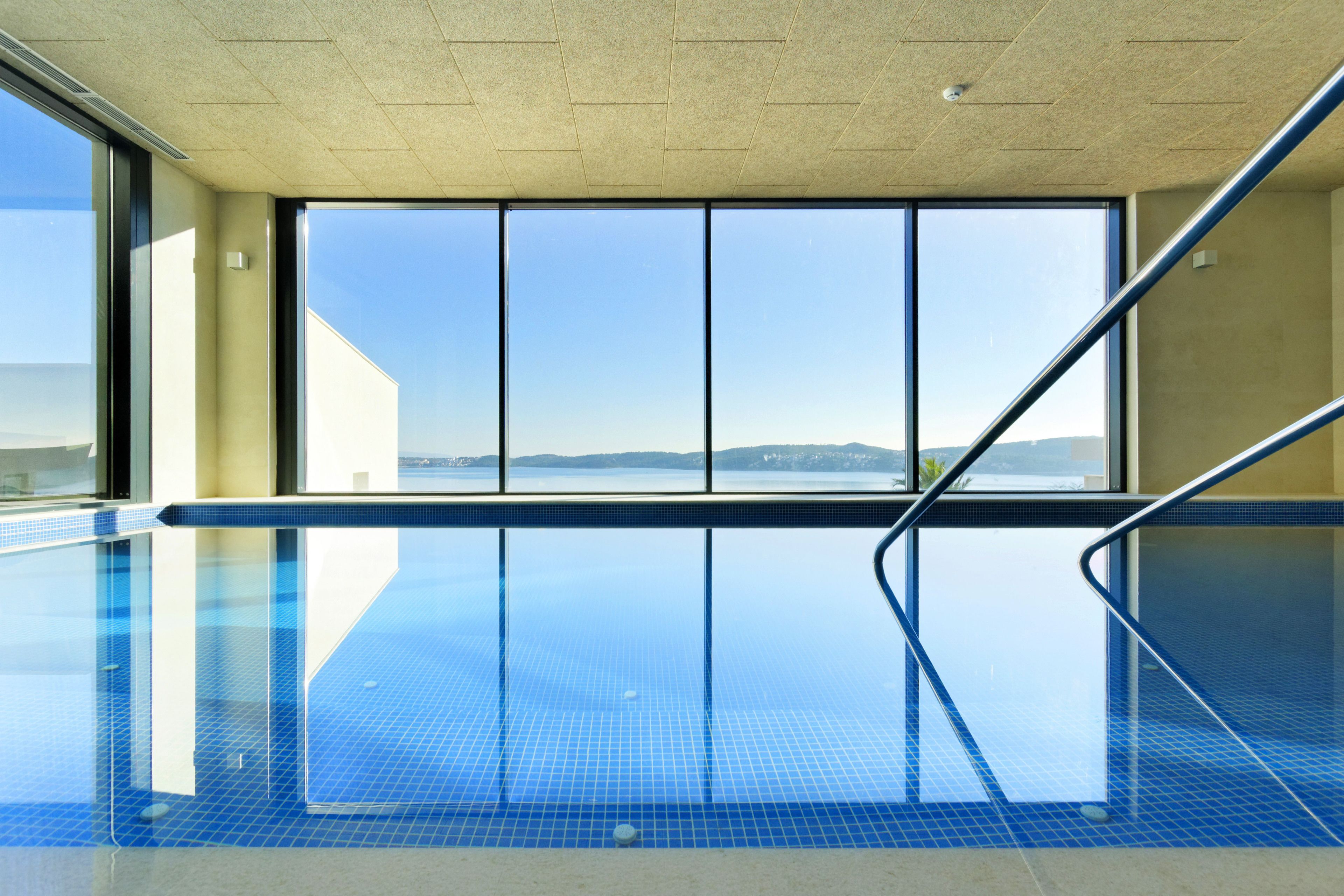 A swimming pool with a clear view of the sea and mountains through large windows.