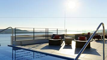 Un área de piscina en la azotea con sillones de descanso y vistas al océano.