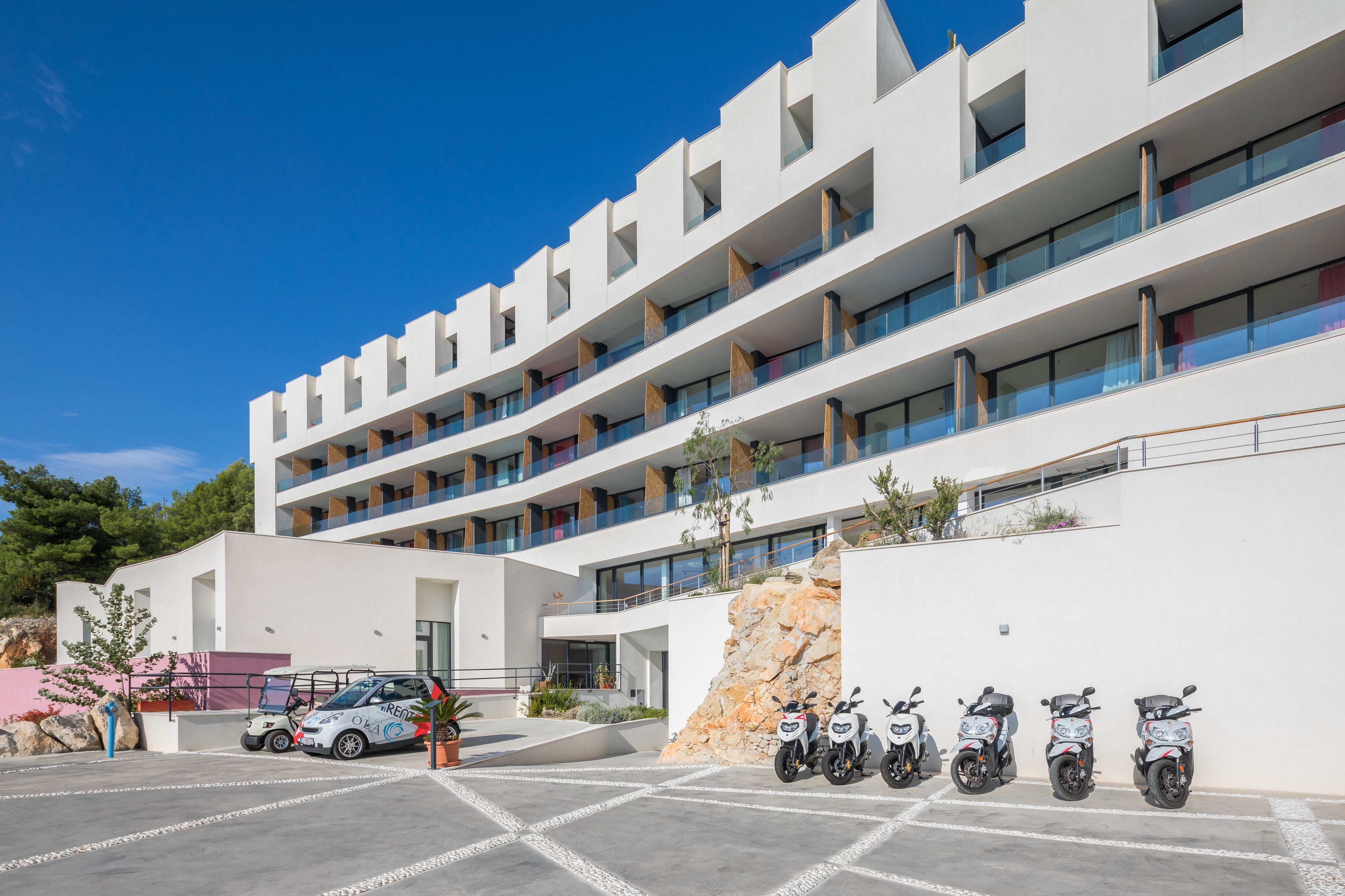 A modern multi-story building with a parking area and several parked scooters.
