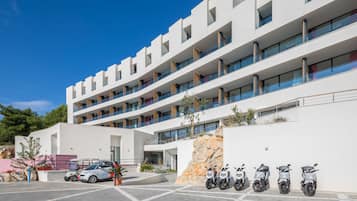 A modern multi-story building with a parking area and several parked scooters.