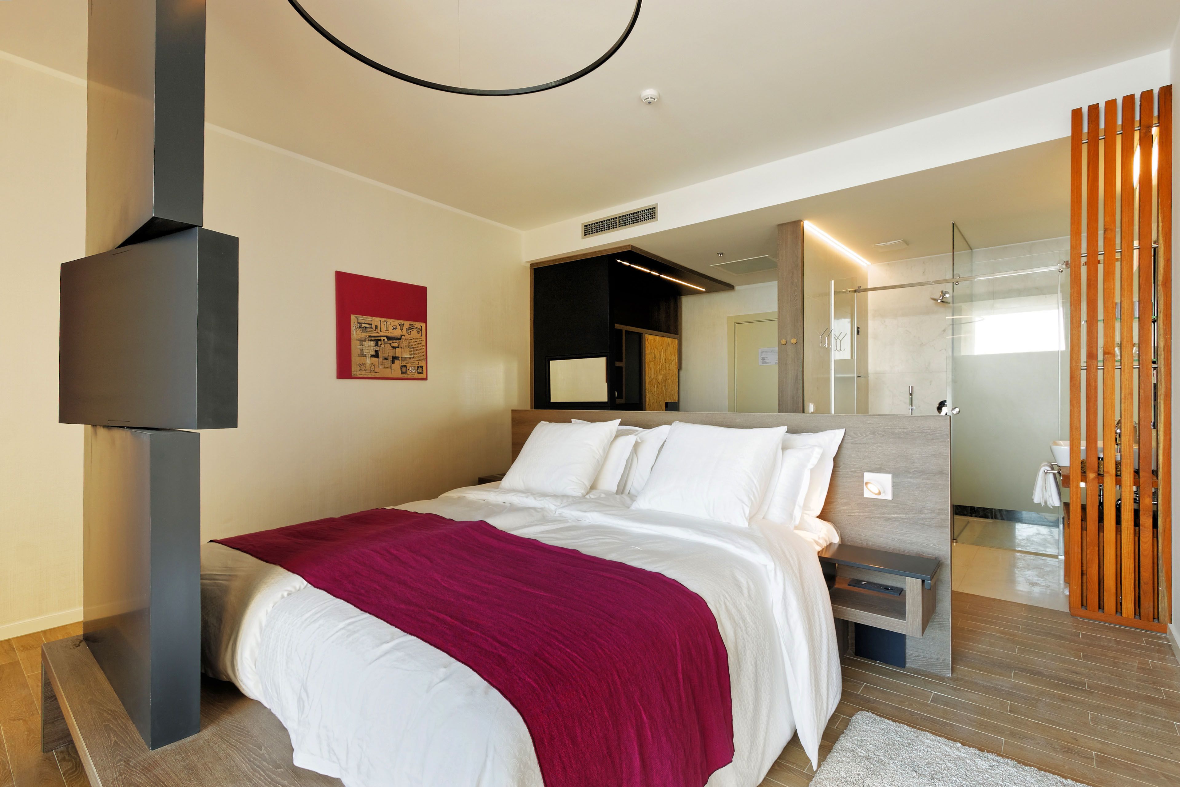 Une chambre d’hôtel moderne dotée d’un grand lit, d’un téléviseur fixé au mur et d’une salle de bain avec une douche à parois de verre.