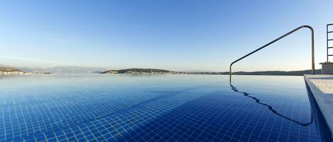 Ein klares, blaues Infinity-Pool mit einer Metallleiter rechts, mit Blick auf eine weit entfernte Landschaft.