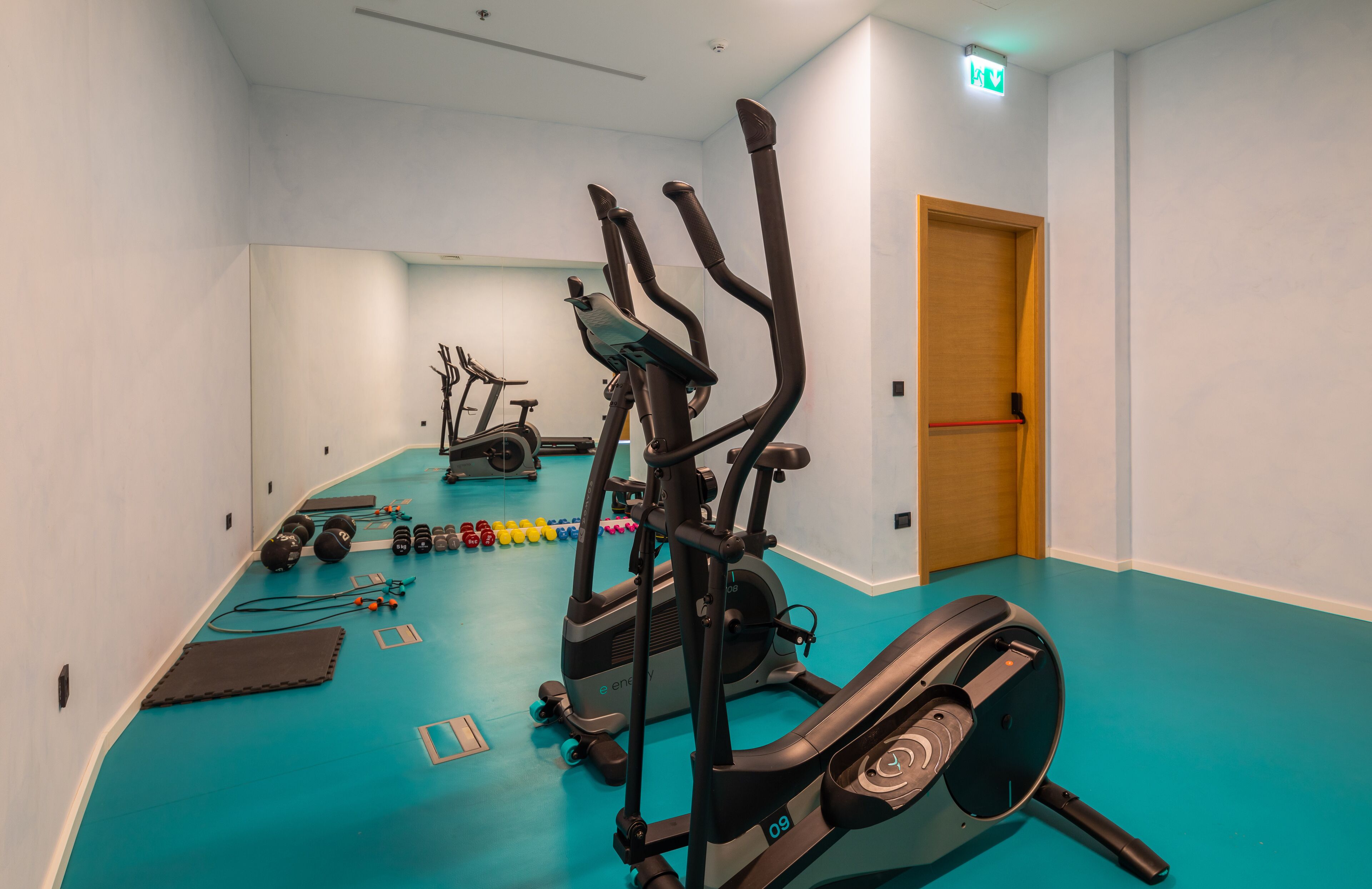 A gym with various exercise equipment, including treadmills and weights, on a blue floor.