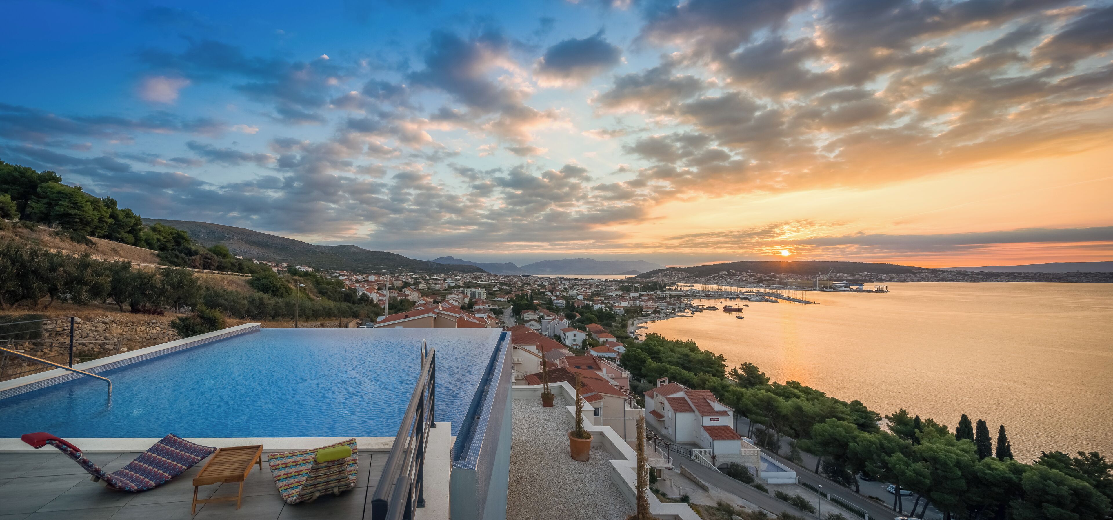 A poolside view overlooking a coastal town with a sunset.