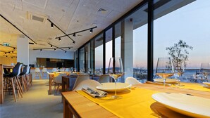 Un restaurante con mesas preparadas para comer, ventanas amplias y vistas del paisaje urbano.