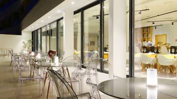 Un comedor moderno con sillas y mesas de plástico transparente, ventanas amplias y un interior bien iluminado.