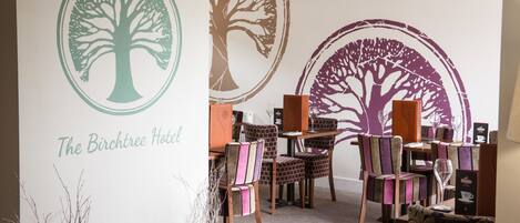 Un vestíbulo de hotel con un mural grande de un árbol, una mesa de recepción y varias sillas.