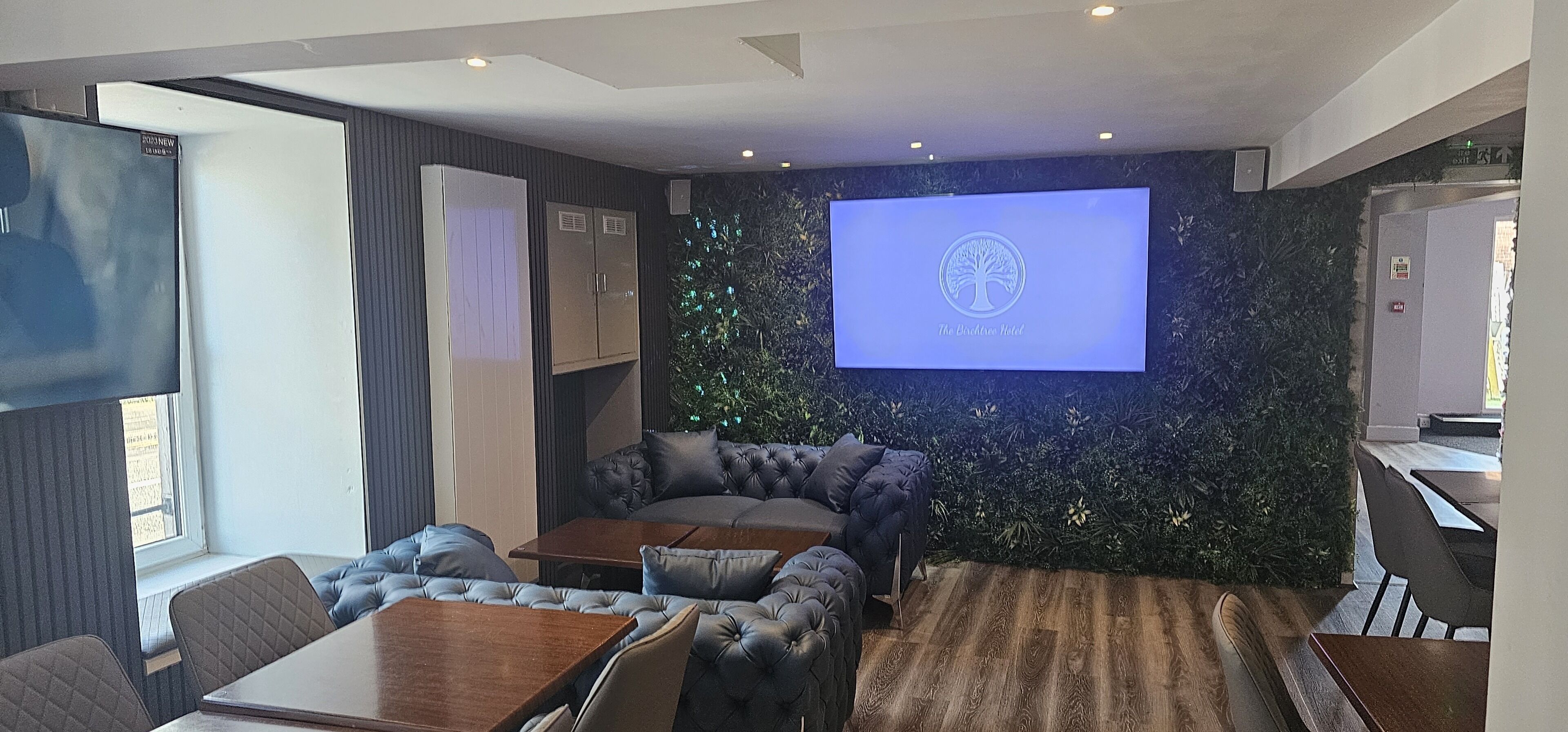 A modern hotel lobby with a large screen displaying the hotel logo, plush seating, and a wooden floor.