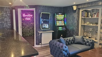 Ett rum med en neonreklamskylt som visar texten ”Buchtree Hotel”, en spelautomat, en soffa och en bokhylla fylld med troféer.