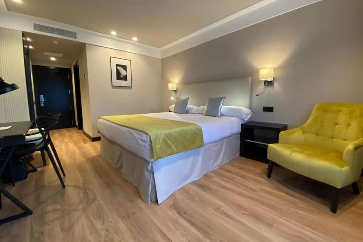 A hotel room with a bed, bedside tables, a chair, and a desk.