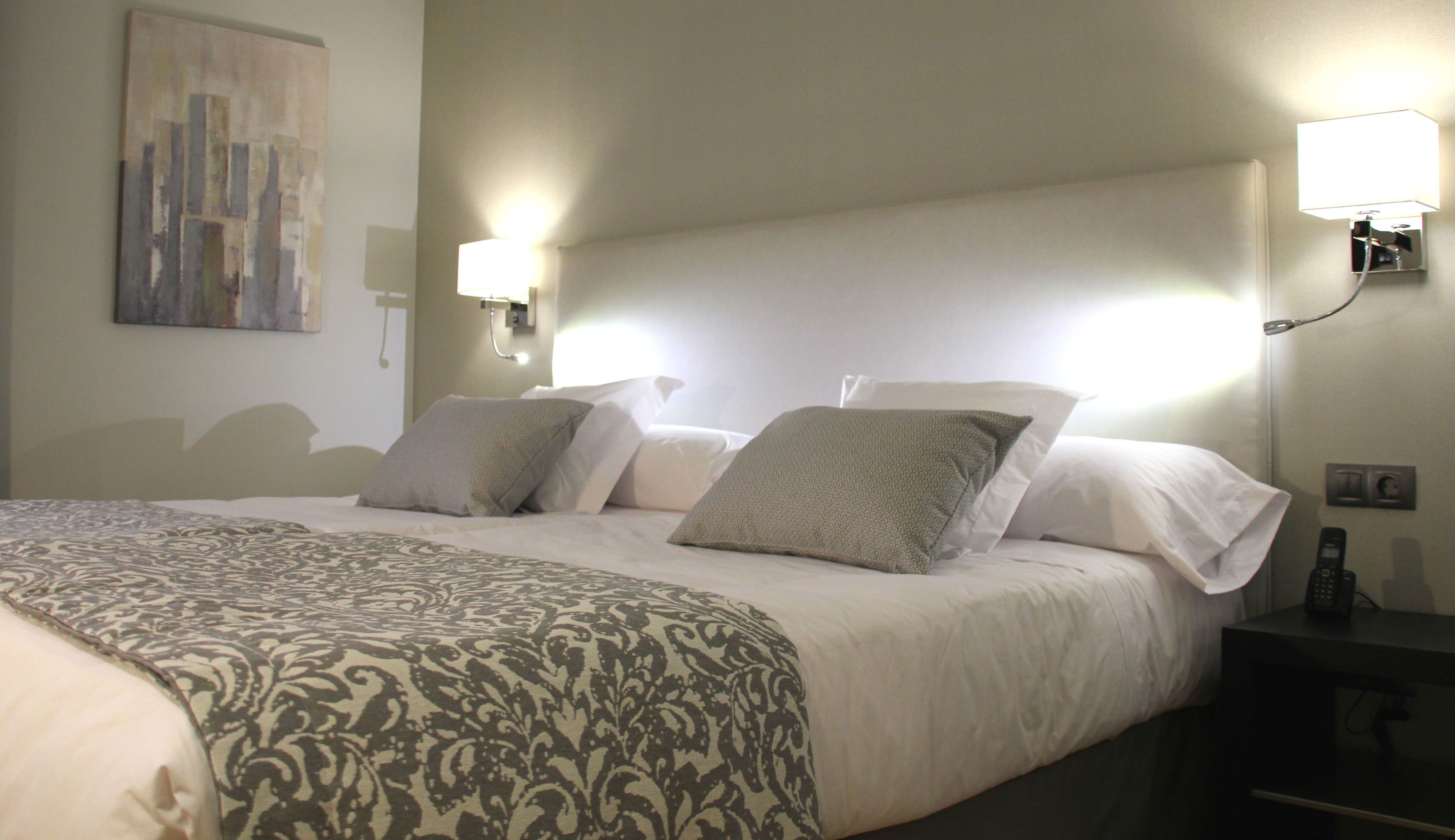 Una habitación de hotel con una cama grande, dos lámparas de noche, un teléfono junto a la cama y un cuadro en la pared.