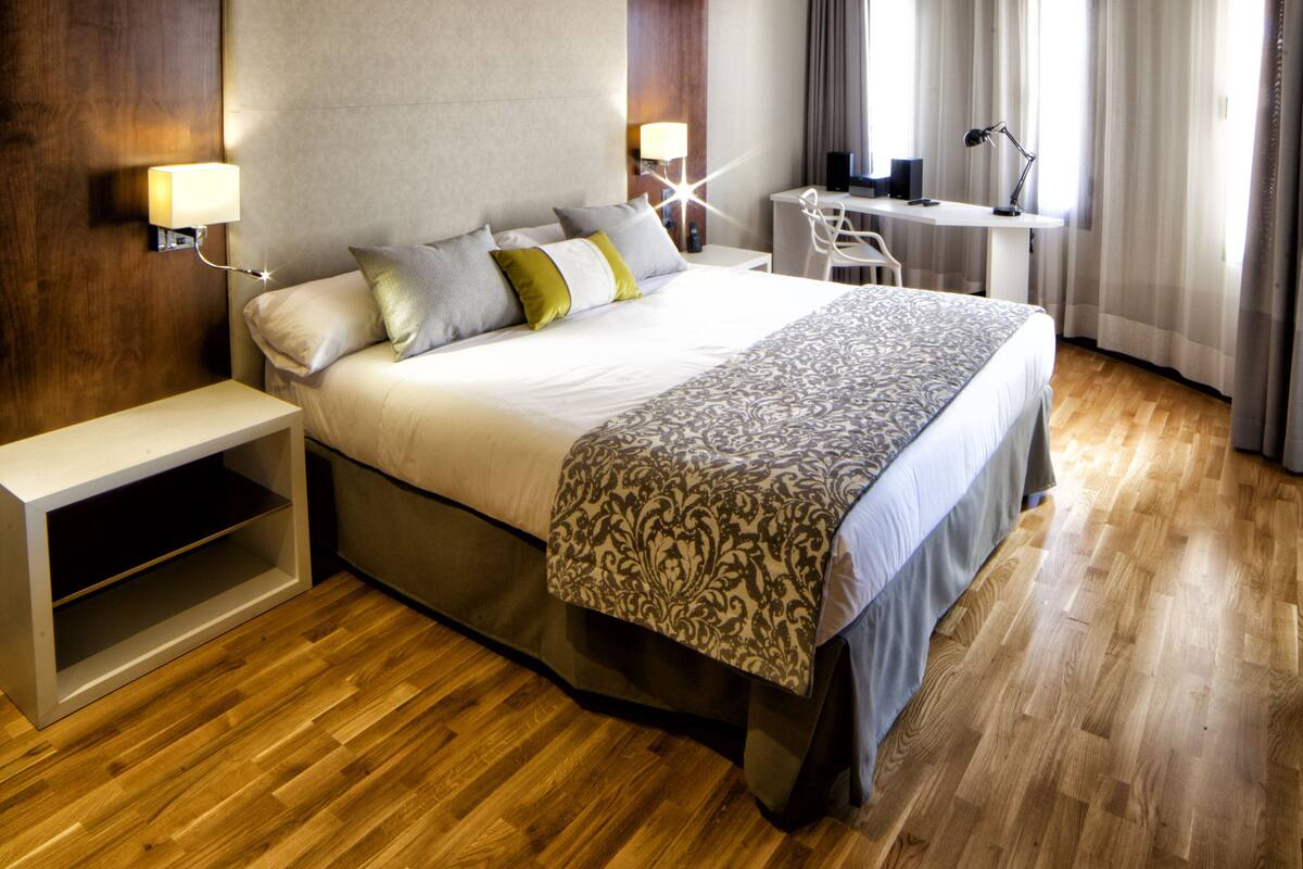 A hotel room with a large bed, bedside tables, a desk, and a chair.