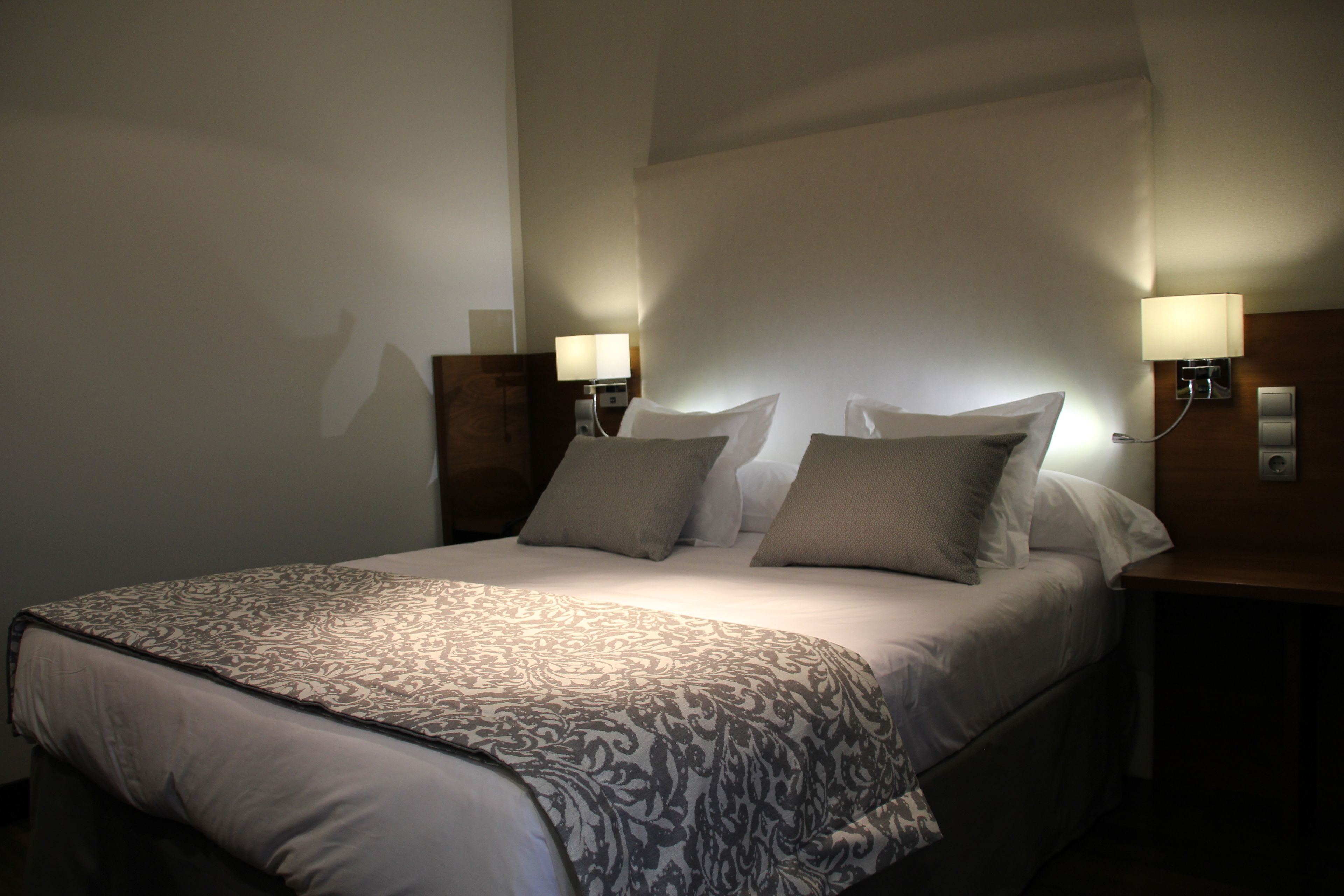 Una camera d'albergo con un letto grande, due lampade da comodino e un comodino.