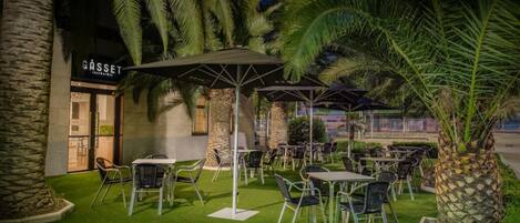 Un área de estar al aire libre con mesas y sillas, palmeras y un edificio con un letrero que dice