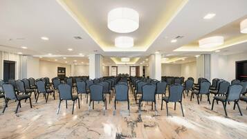 Une salle de conférence avec des rangées de chaises, un sol en marbre et un éclairage encastré.
