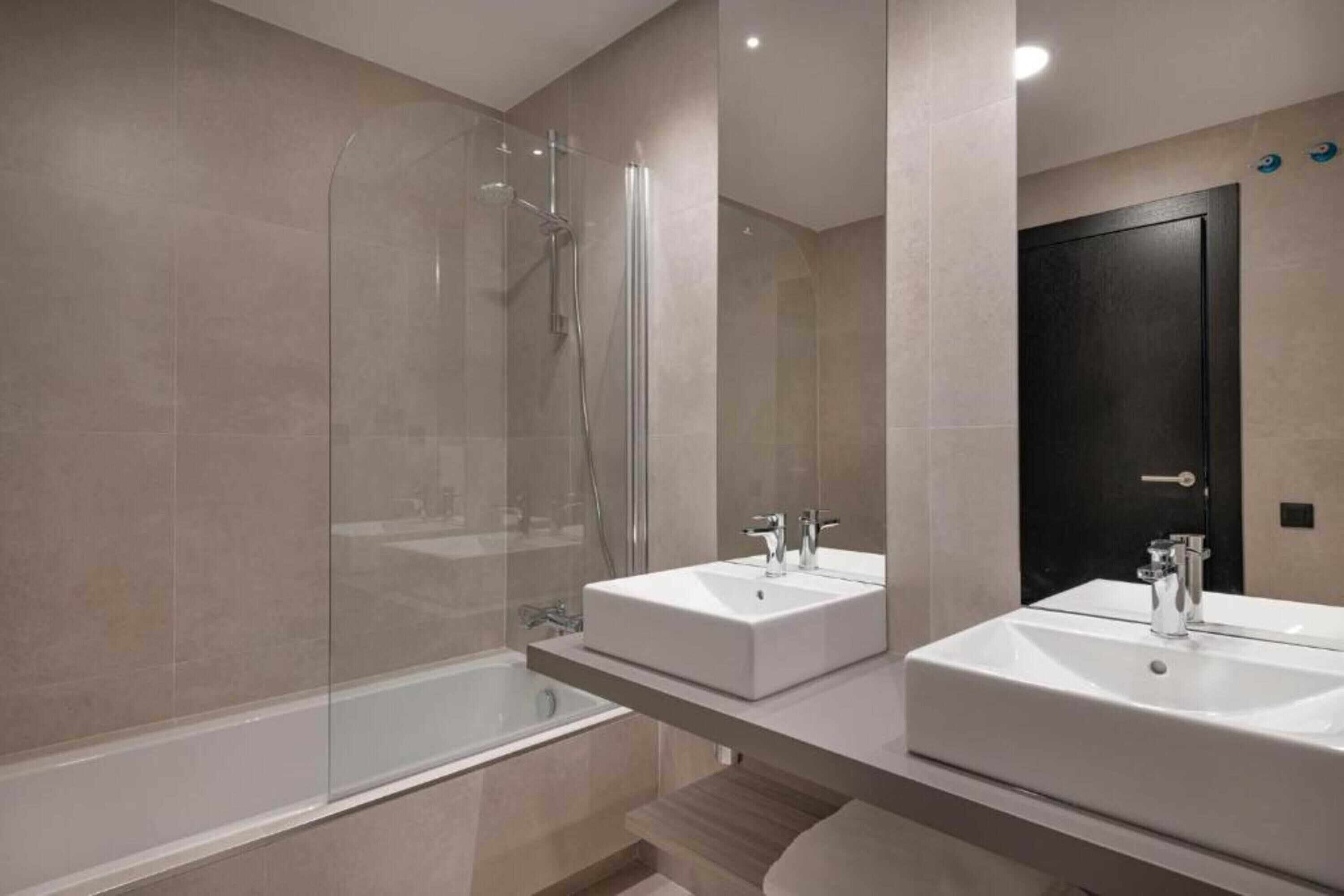 Un bagno moderno con doccia vetro, due lavabi e una porta scura.