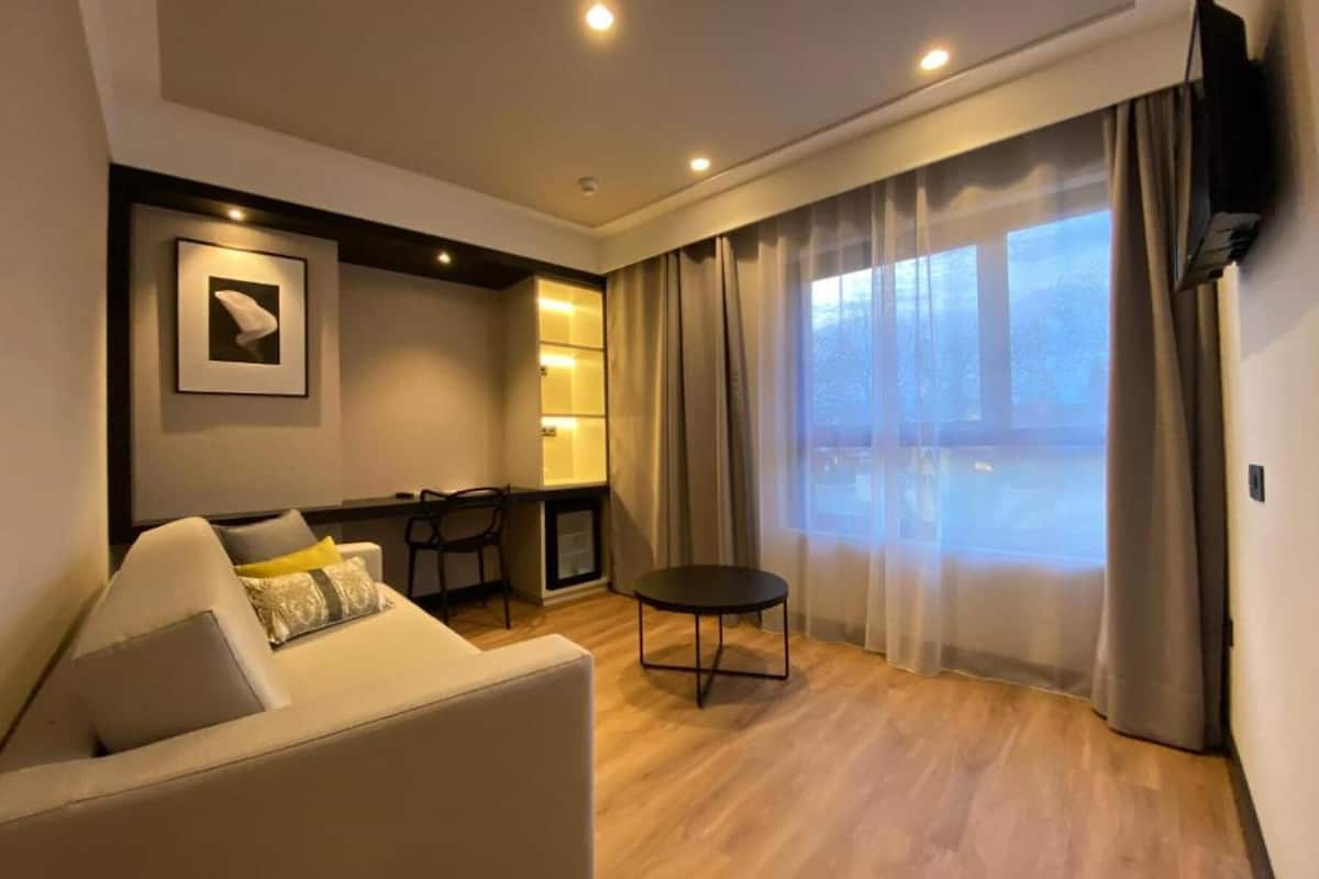 A modern living room with a sofa, a small table, and a view of the outdoors through large windows.