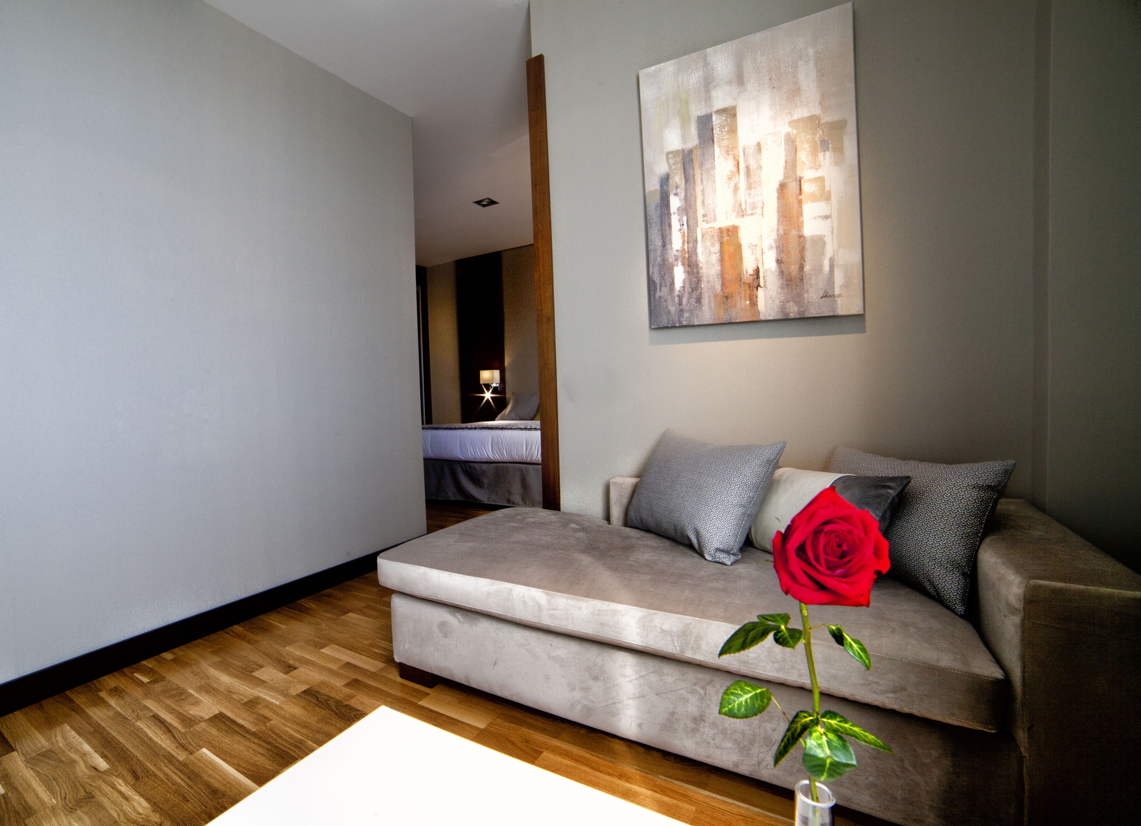 Una sala de estar moderna con un sofá gris, una rosa roja en un florero y un cuadro en la pared.