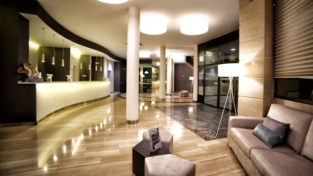 Un hall d  ’entrée moderne comprenant un comptoir d’accueil, un espace salon et un escalier menant aux étages supérieurs.