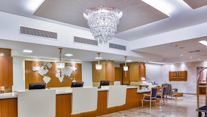 A hotel reception area with a marble floor, a large chandelier, and a reception desk with a world map mural. - Mendes Plaza Hotel Torre Panorama (Santos)