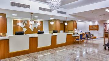 Um hall de recepção de hotel com piso de mármore, um grande lustre e um balcão de atendimento com um mural de mapa-múndi.